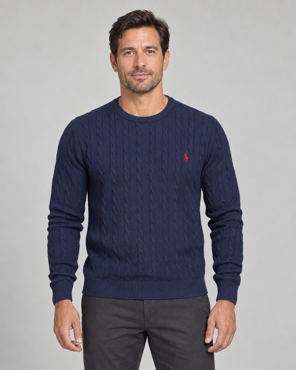 Front cropped view of a man wearing a dark blue cable-knit crew-neck jumper with a small red chest motif.