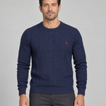 Front cropped view of a man wearing a dark blue cable-knit crew-neck jumper with a small red chest motif.
