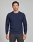 Front cropped view of a man wearing a dark blue cable-knit crew-neck jumper with a small red chest motif.
