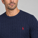 Close-up of a man wearing a dark blue cable-knit crew-neck jumper with red chest embroidery