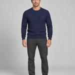 Front full-body view of a man wearing a dark blue cable-knit crew-neck jumper with a small red chest motif.