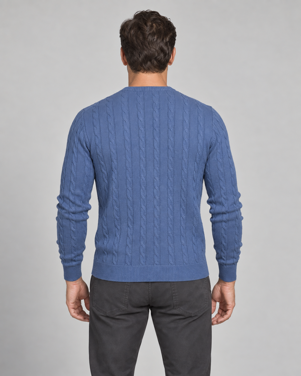 Back view of a man wearing a blue cable-knit crew-neck jumper with ribbed cuffs and hem