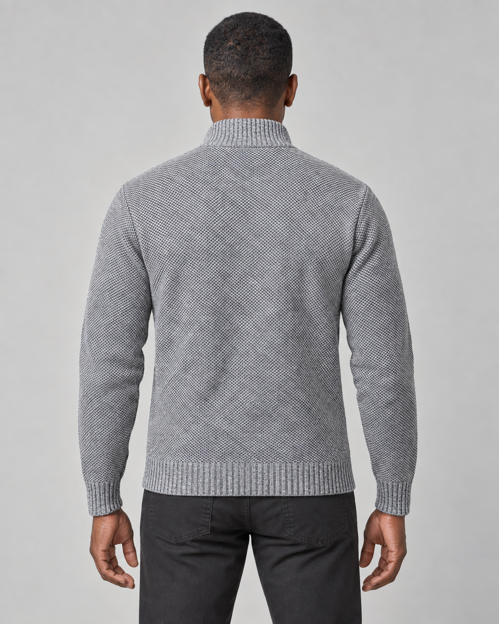 Back view of a light grey textured sweater with a ribbed high neck, cuffs and hem, worn with black trousers.