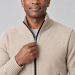 Close-up of a light khaki textured zip-up jumper with a ribbed high collar and black zip detailing.
