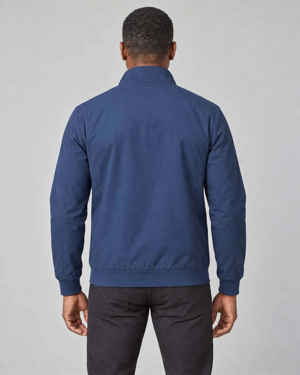 Back view of a man wearing a blue jacket with a raised collar, long sleeves, ribbed cuffs and hem.