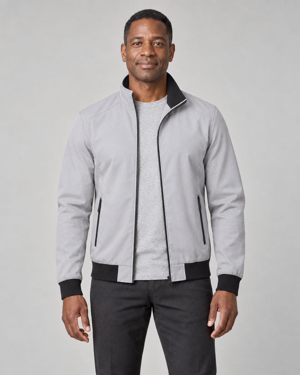 Front cropped view of a man wearing an open grey jacket with black trim and zipped side pockets.