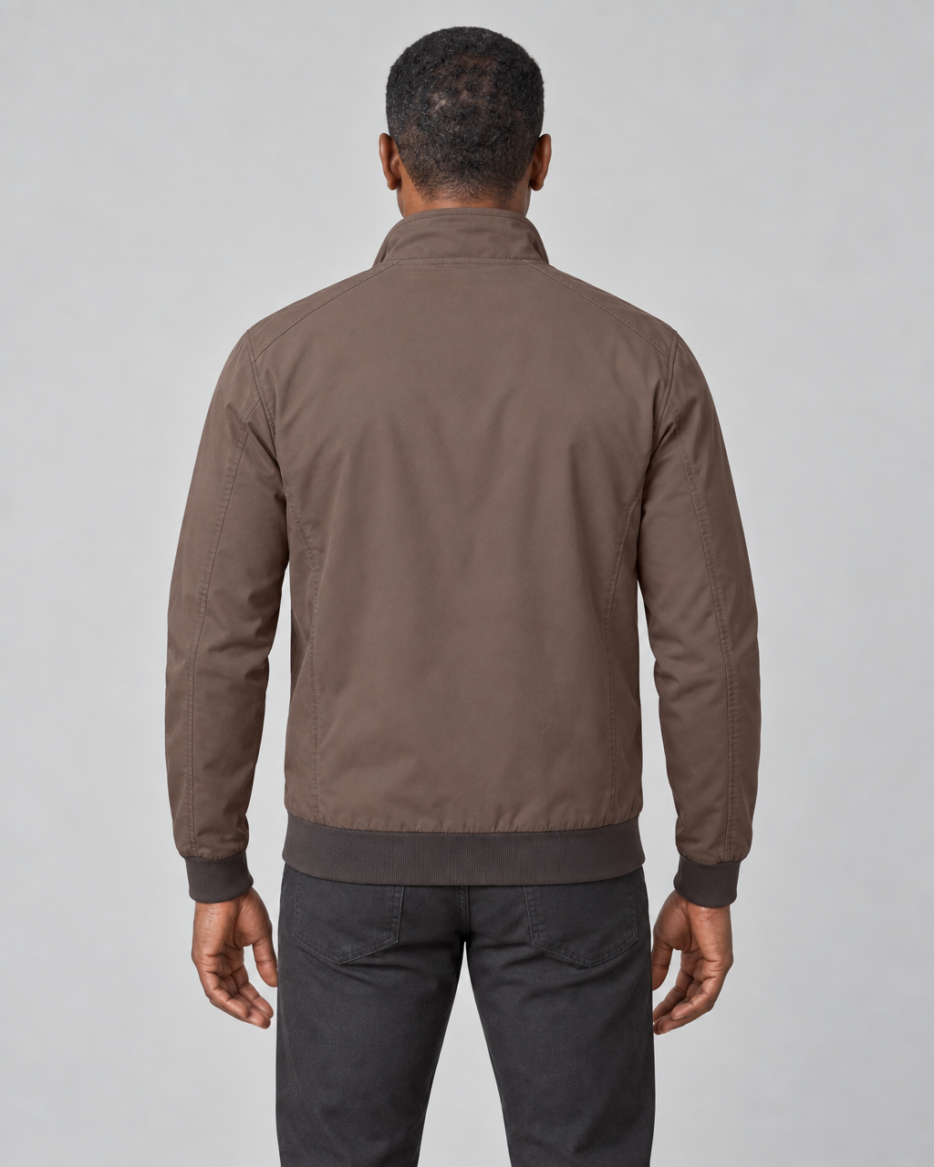 Back view of a model wearing a brown jacket with a raised collar and dark ribbed cuffs and hem.