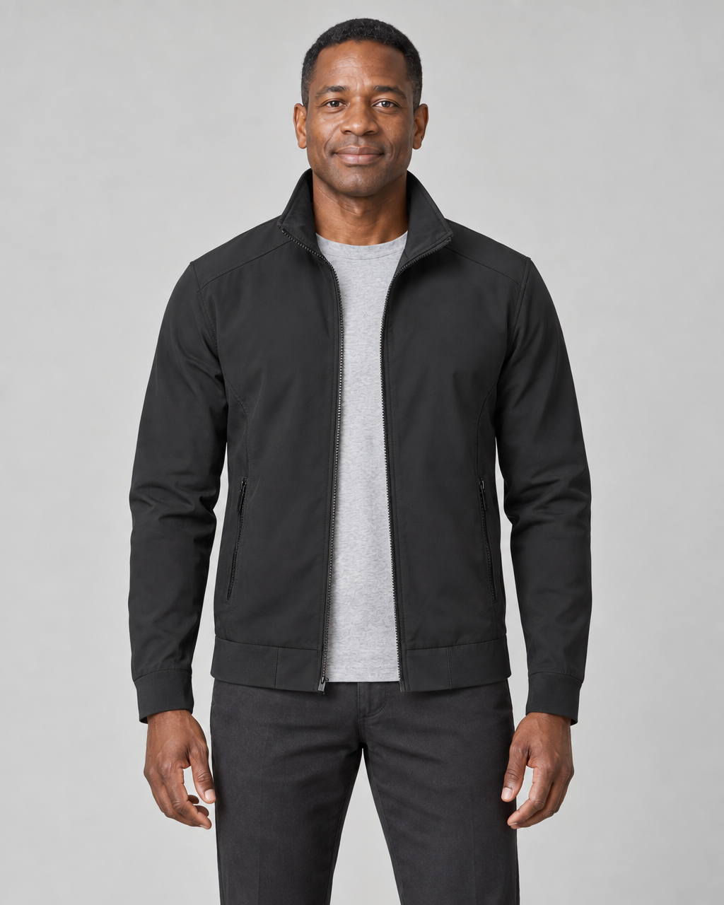 Front cropped view of a man wearing an open black zip-up jacket with a stand collar and zipped side pockets