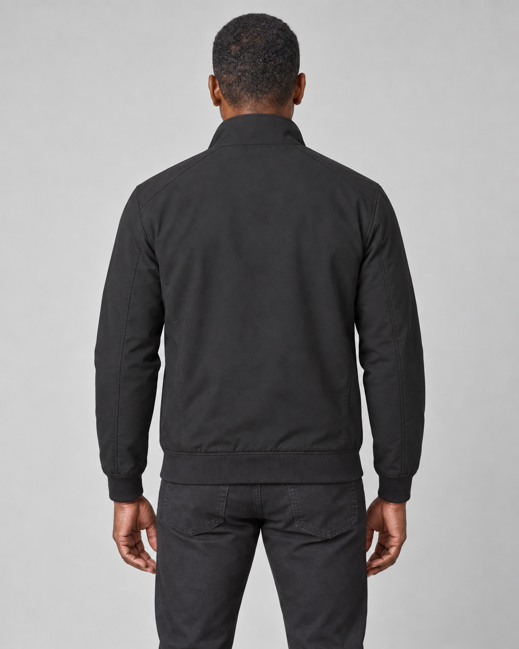 Cropped back view of a model wearing a black jacket with a raised collar and ribbed hem and cuffs