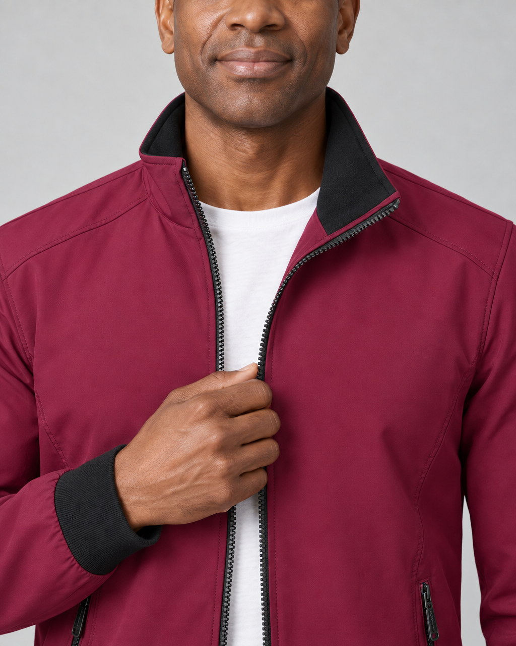 Close-up front view of a burgundy red jacket with a black-lined stand collar, black cuffs and zip fastening