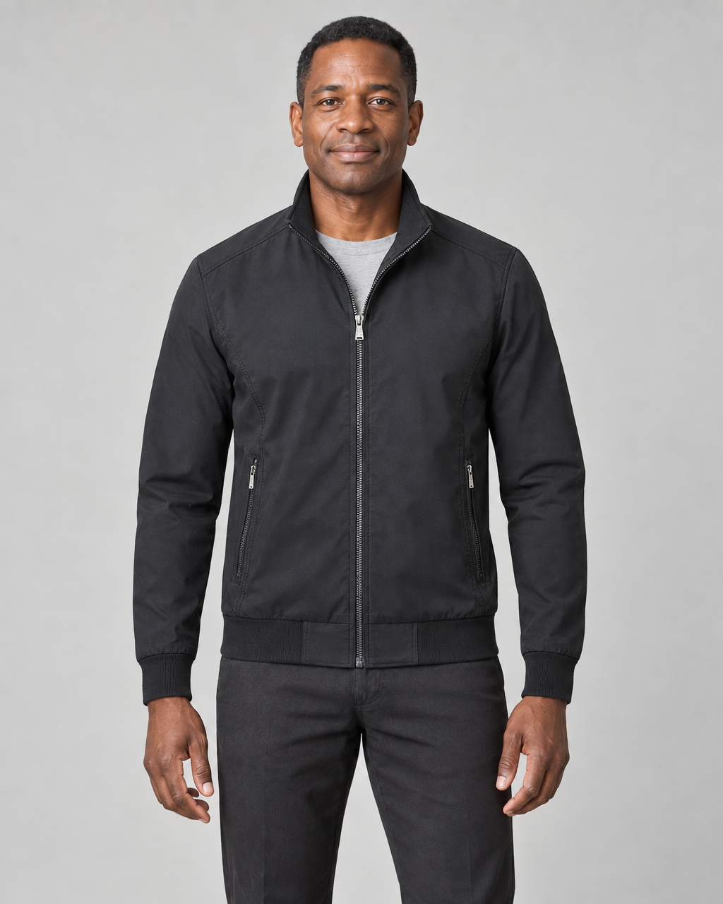Man wearing a black zip-up jacket with a stand collar, ribbed cuffs and hem, and two zipped pockets, front view
