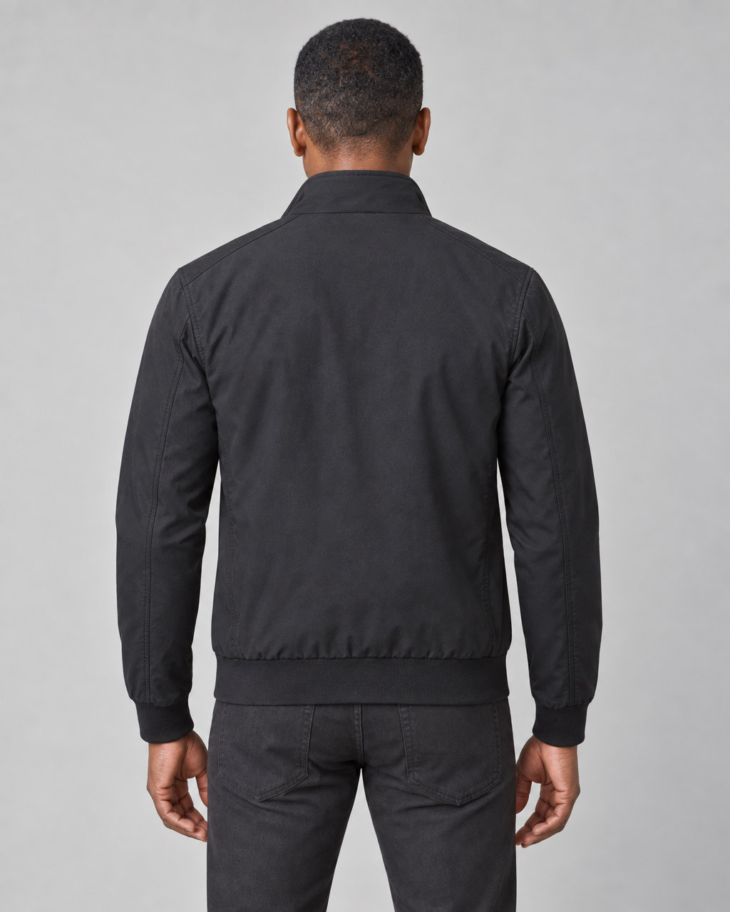 Back view of a man wearing a black jacket with a raised collar, ribbed cuffs and hem
