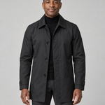 Front cropped view of a man wearing a black thigh-length coat with a pointed collar, buttons, side pockets and cuff tabs.