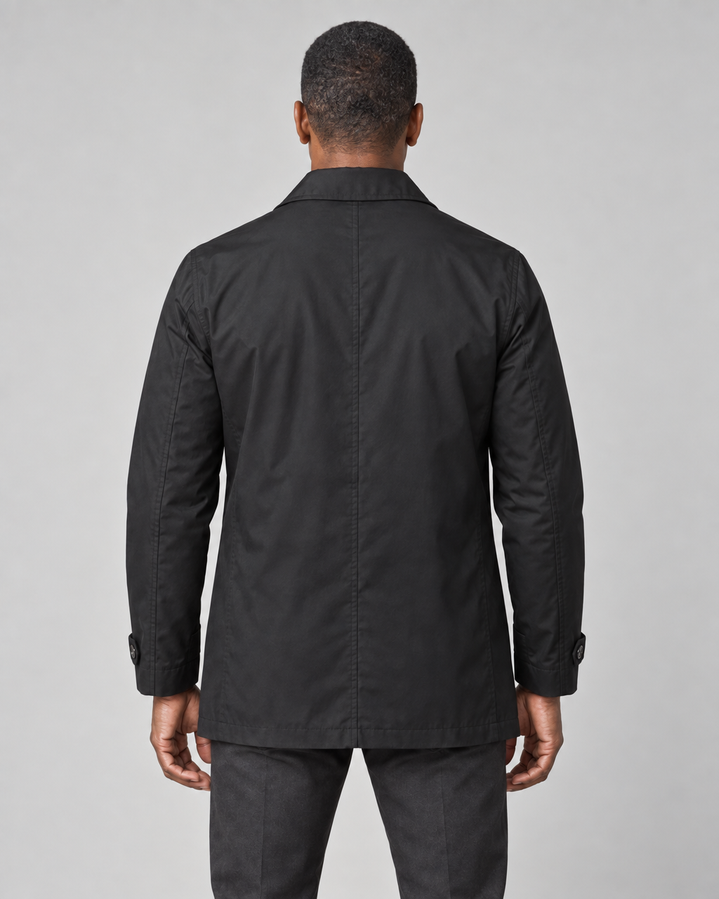 Model shown from behind wearing a black mid-length coat with a pointed collar and button-tab cuffs.